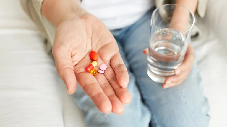 A close-up image of a person's hand holding a selection of colorful pills and a glass of water.