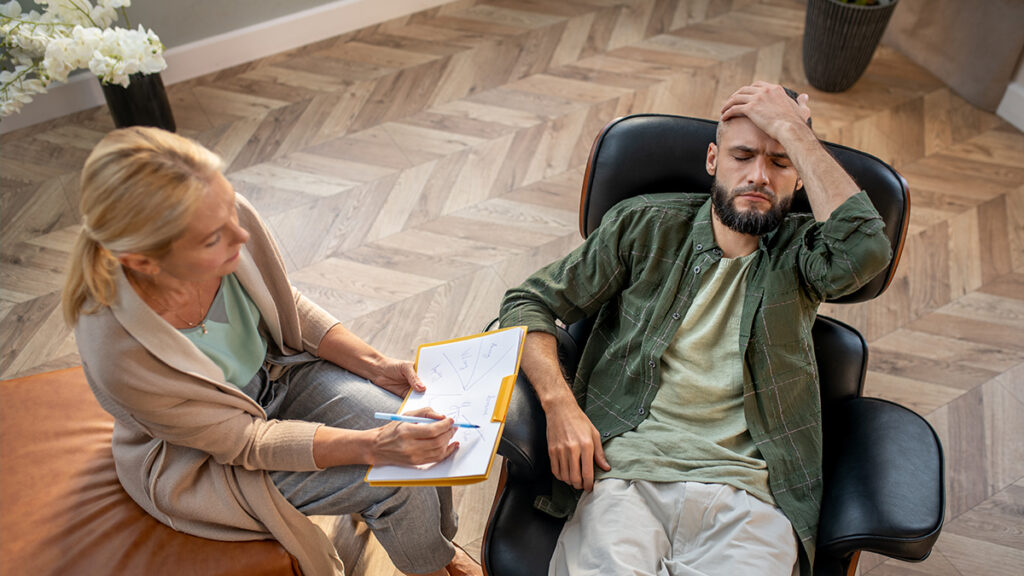 worried man with his head on his forehead speaking to a therapist